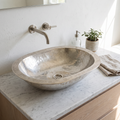 Oval German silver vessel sink with engraved double rim on a white marble vanity with a wall-mounted spout