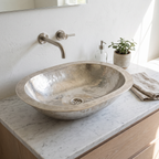Oval German silver vessel sink with engraved double rim on a white marble vanity with a wall-mounted spout