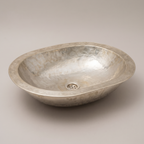 Low oval German silver vessel sink with engraved rim and hammered basin on a plain background