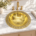 Engraved round brass drop-in sink in a sunlit white marble bathroom vanity