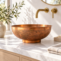Engraved round copper vessel sink on a sunlit white marble bathroom vanity