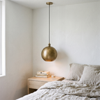 Hammered brass globe pendant hanging beside a bed in a white plaster bedroom