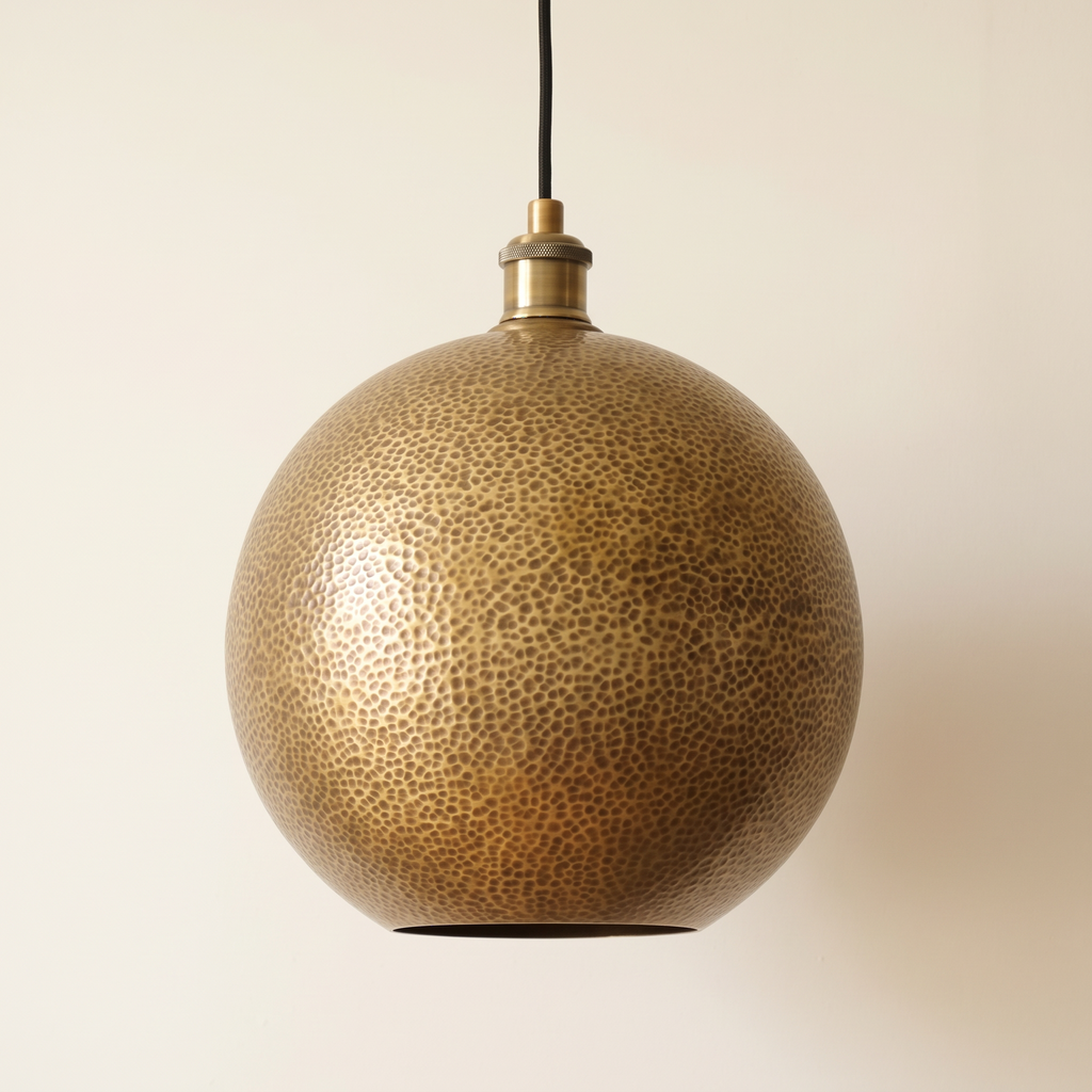 Hammered brass globe pendant with open bottom and black cord on a light background