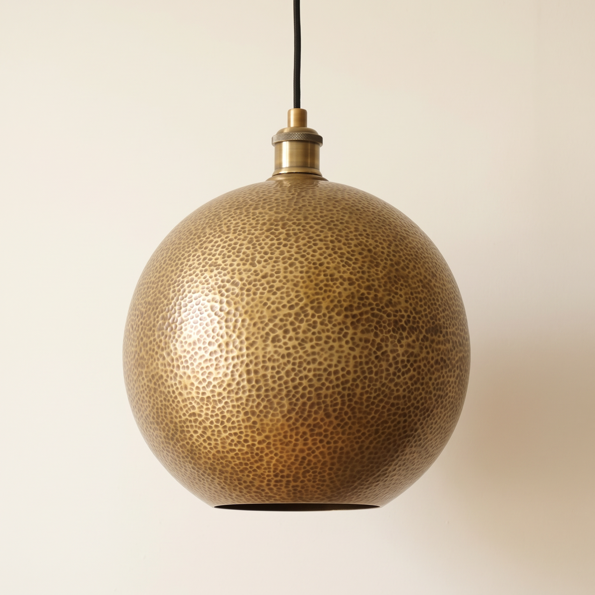 Hammered brass globe pendant with open bottom and black cord on a light background