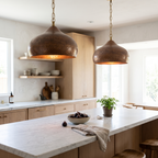 Two hammered antique copper bell pendant lights on brass chains over a white marble kitchen island