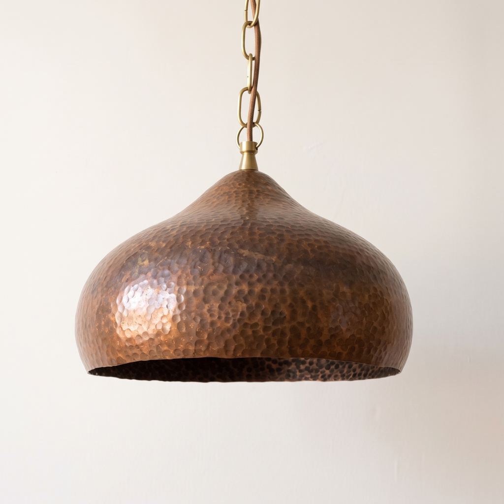 Onion-shaped hammered copper pendant with antique finish on a brass chain, light background