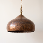 Onion-shaped hammered copper pendant with antique finish on a brass chain, light background