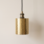 Hammered unlacquered brass cylinder pendant with antique brass socket on a light background