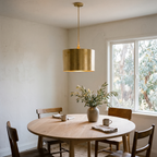 Hammered brass drum pendant light over a round white oak dining table