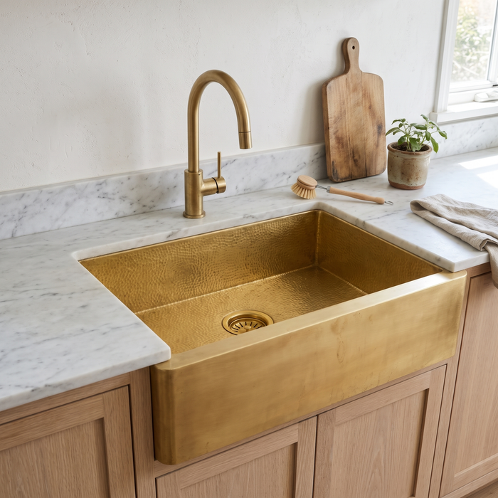 Hammered brass farmhouse apron sink with brass basket strainer in a white oak kitchen