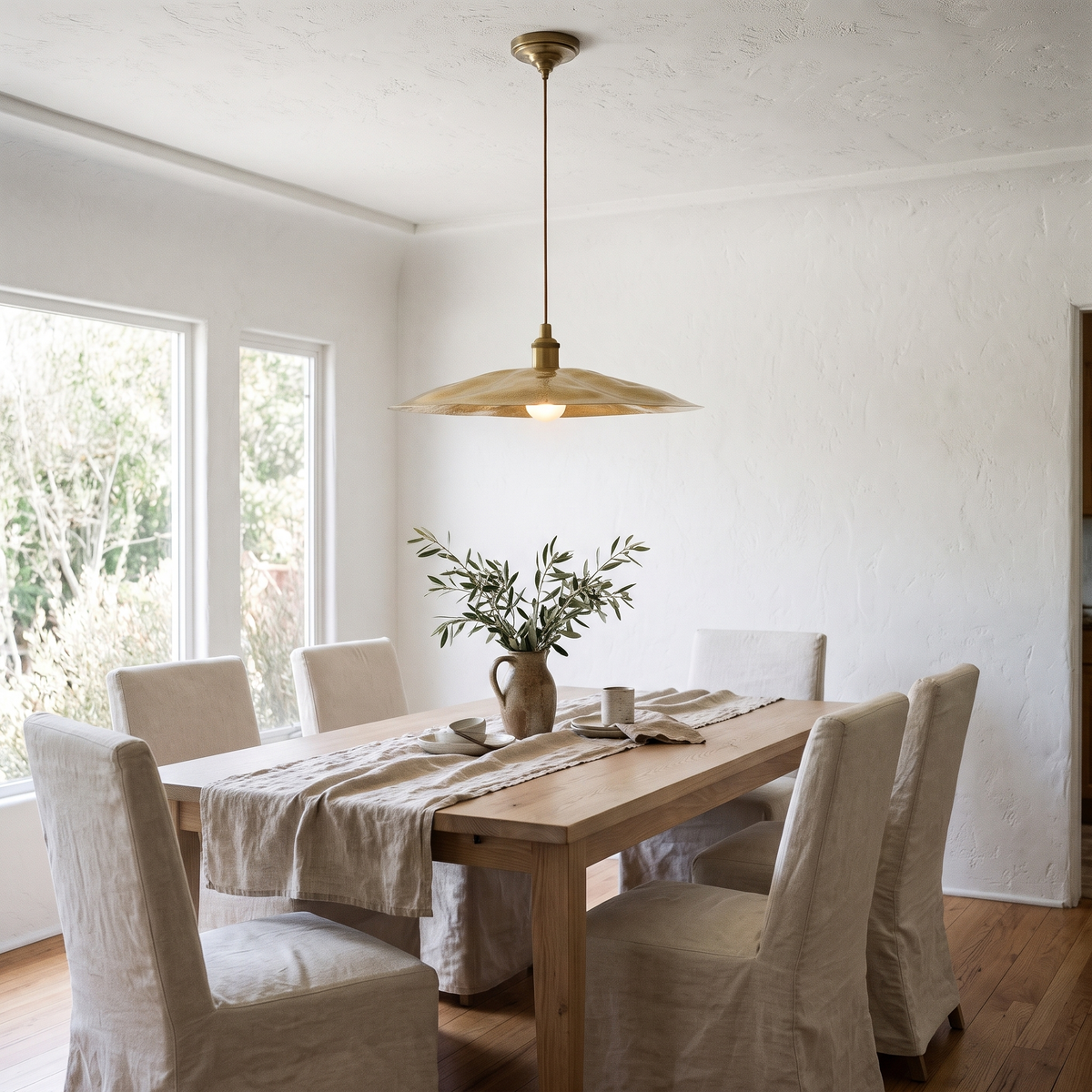 Hammered brass flat disc pendant light over a white oak dining table