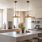 Two hammered brass flat disc pendant lights over a white marble kitchen island