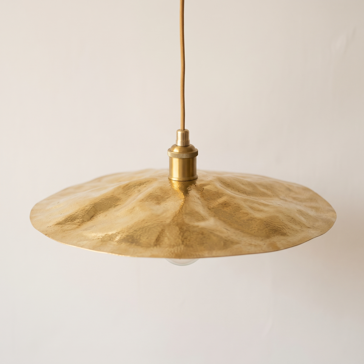 Hammered brass flat disc pendant light with rippled unlacquered brass shade on a light background