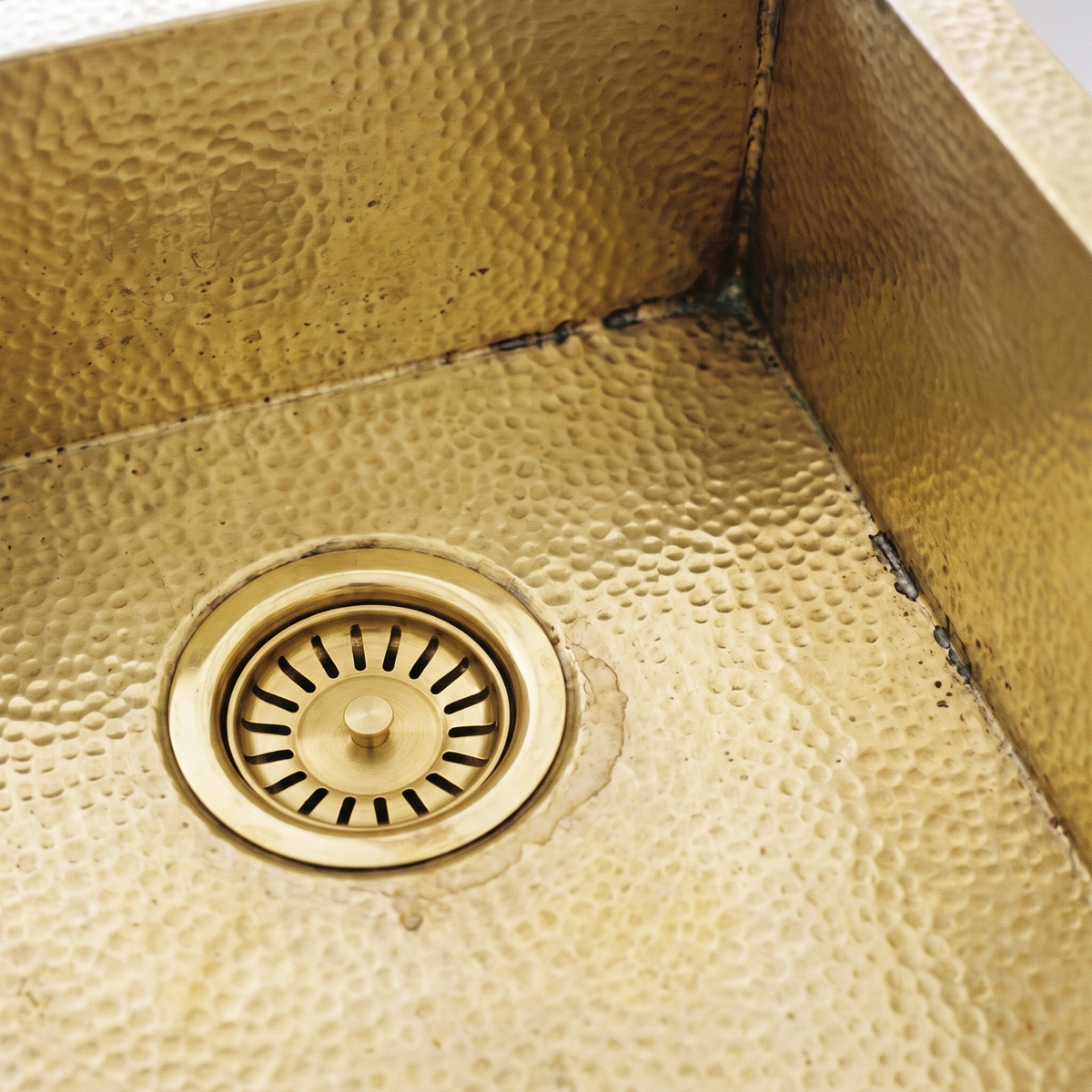 Close-up of the hammered brass corner and brass basket strainer drain of a rectangular sink