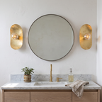 Pair of hammered brass oval plate wall sconces beside a round powder room mirror