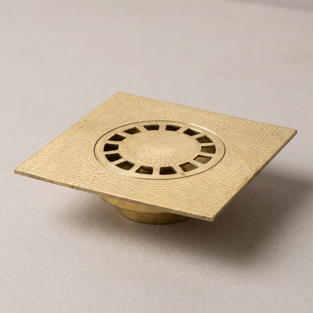Hammered brass square floor drain with round slotted grate on a light background