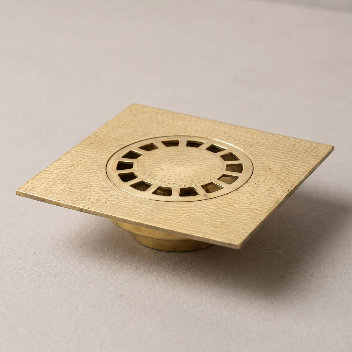 Hammered brass square floor drain with round slotted grate on a light background