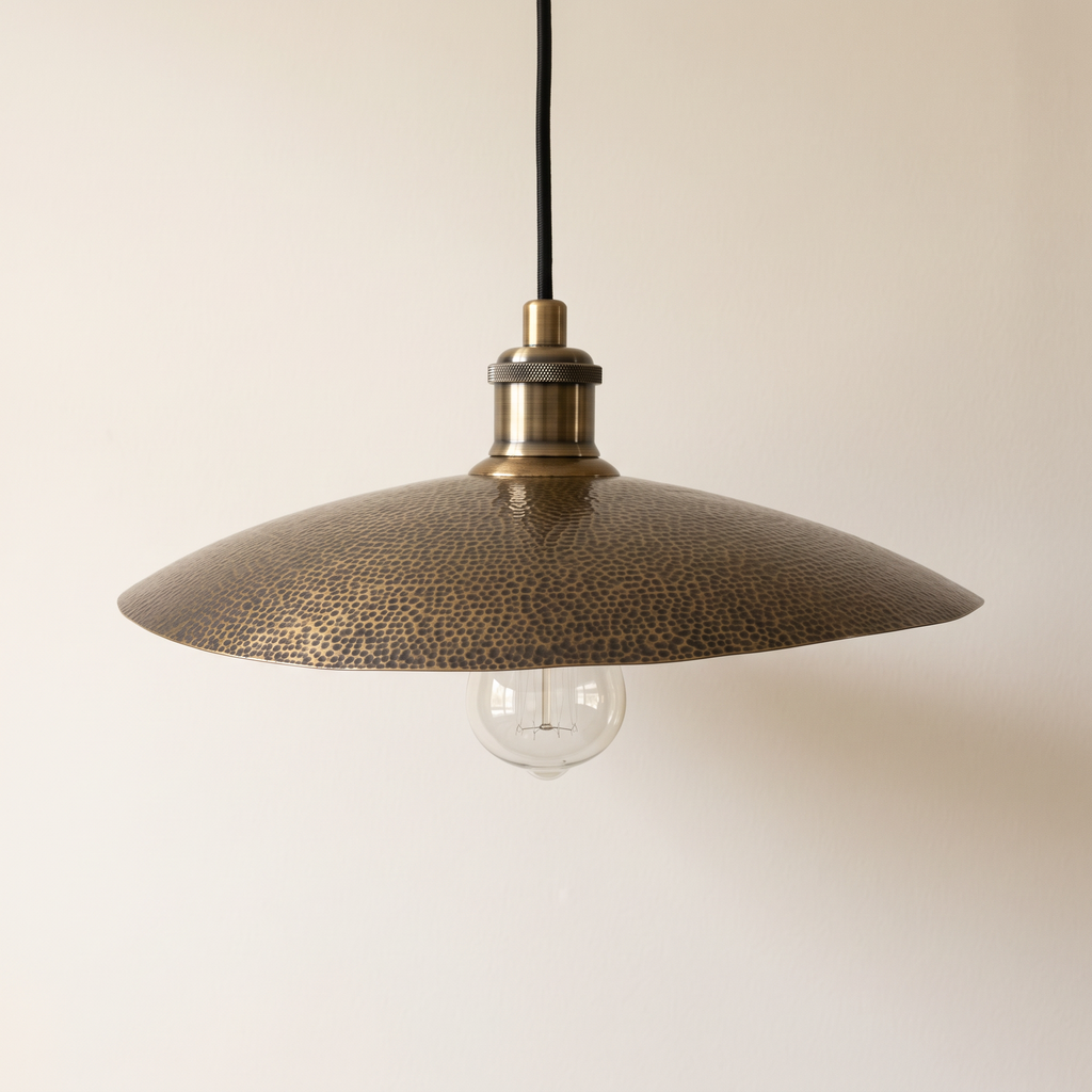 Hammered brass saucer pendant with filament bulb and black cord on a light background