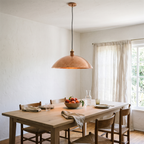 Hammered copper wide dome pendant over a white oak dining table