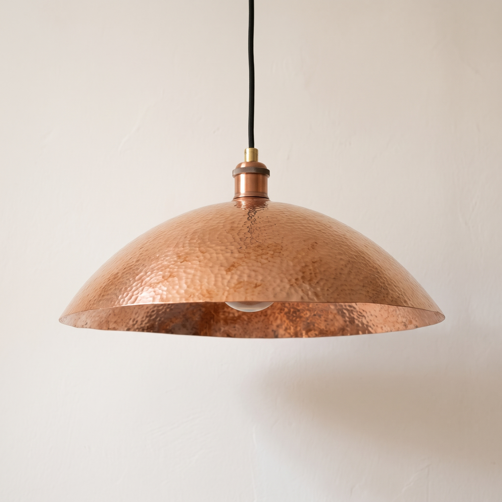 Hammered unlacquered copper wide dome pendant with black cord on a light background