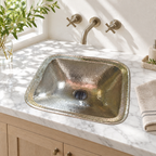 Hammered German silver rectangular drop-in sink in a sunlit white marble bathroom vanity