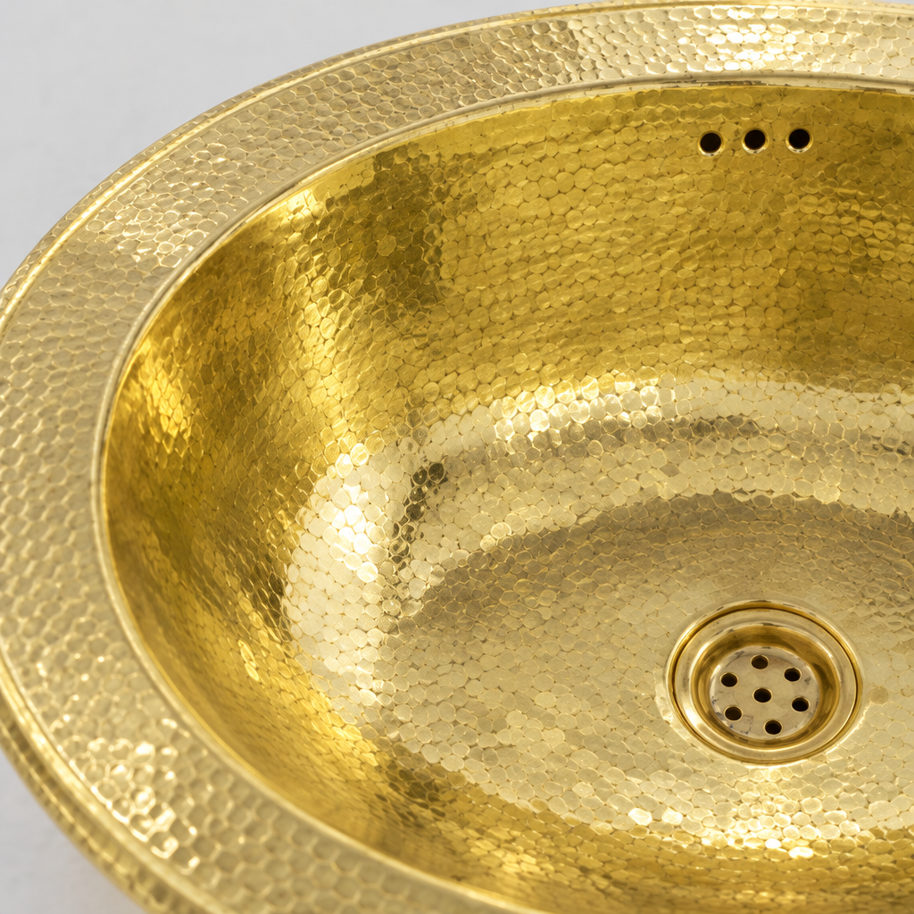 Close-up of the hammered oval brass drop-in sink with overflow showing the finish