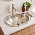 Hammered oval German silver drop-in sink set in a white marble vanity with a brushed nickel faucet