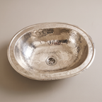 Oval German silver drop-in sink with stepped rim, overflow holes and drain basket on a plain background