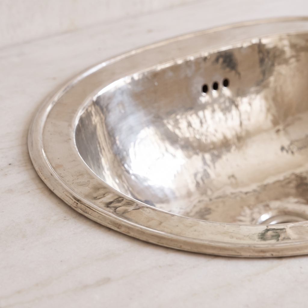 Close-up of the stepped rim, hammered facets and overflow holes of a German silver sink