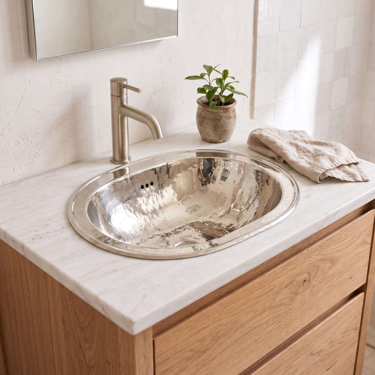 German silver oval drop-in sink on a white oak vanity in a bright guest bathroom