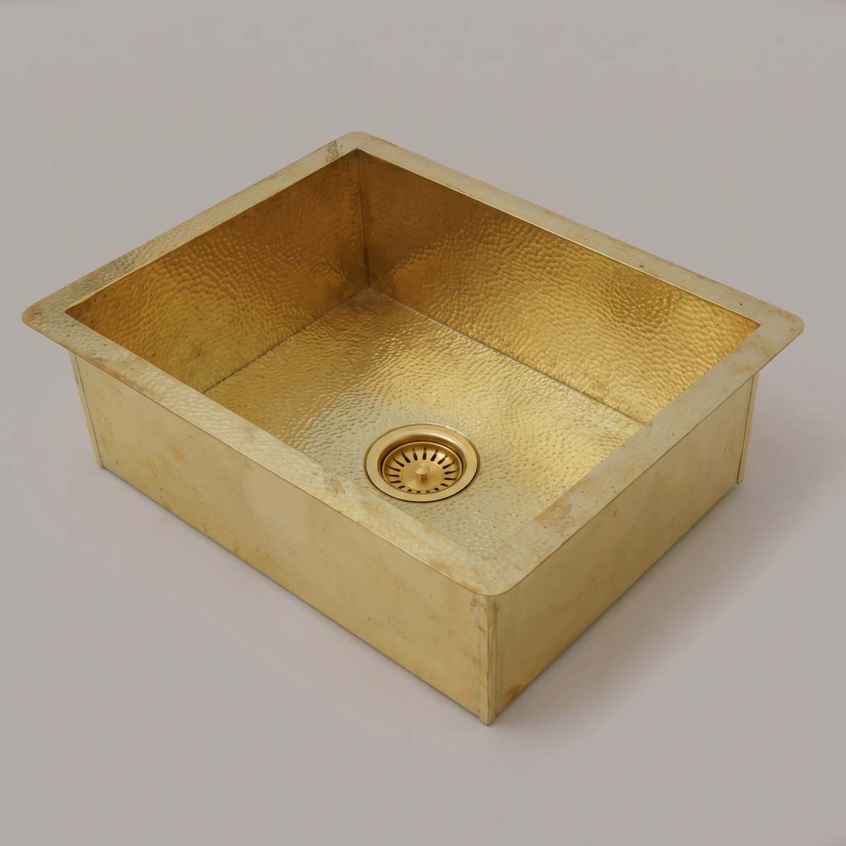 Rectangular brass undermount sink with hammered flange and brass basket strainer on a plain background