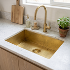 Hammered rectangular brass undermount kitchen sink with brass basket strainer in a white marble counter