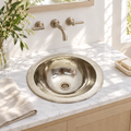 Hammered round German silver drop-in sink in a sunlit white marble bathroom vanity