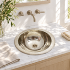 Hammered round German silver drop-in sink in a sunlit white marble bathroom vanity
