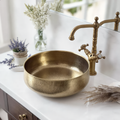 Brass vessel sink on a white marble bathroom vanity with a brass tap