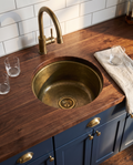 Hand-hammered unlacquered brass bar sink installed undermount in a walnut butcher block counter in an American home wet bar
