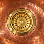 Close-up of a brass sink strainer flange in a hammered copper basin