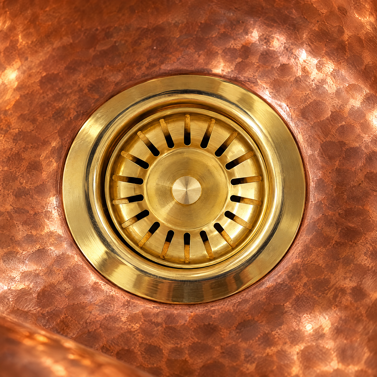 Close-up of a brass sink strainer flange in a hammered copper basin