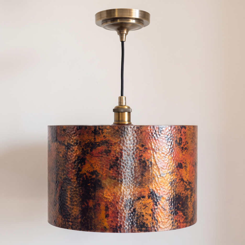 Copper drum pendant with fire-oxidized patina, antique brass socket and canopy, on a light background