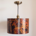 Copper drum pendant with fire-oxidized patina, antique brass socket and canopy, on a light background