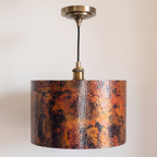 Copper drum pendant with fire-oxidized patina, antique brass socket and canopy, on a light background