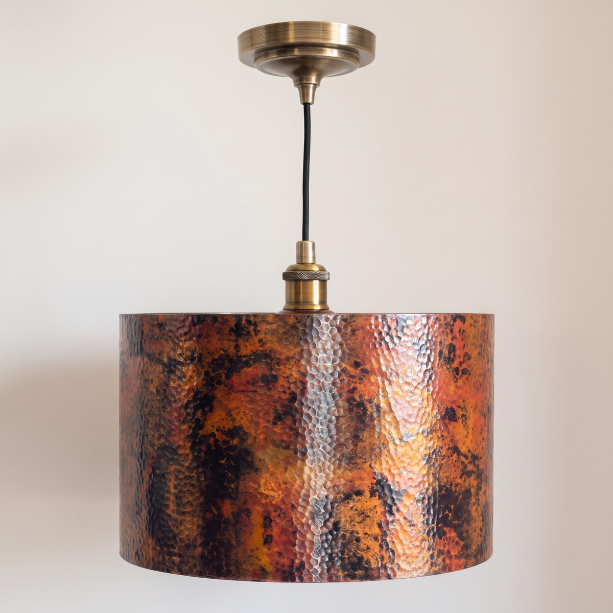 Copper drum pendant with fire-oxidized patina, antique brass socket and canopy, on a light background