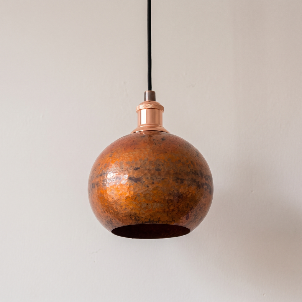Hammered oxidized copper globe pendant with copper socket cup and black cord, light background