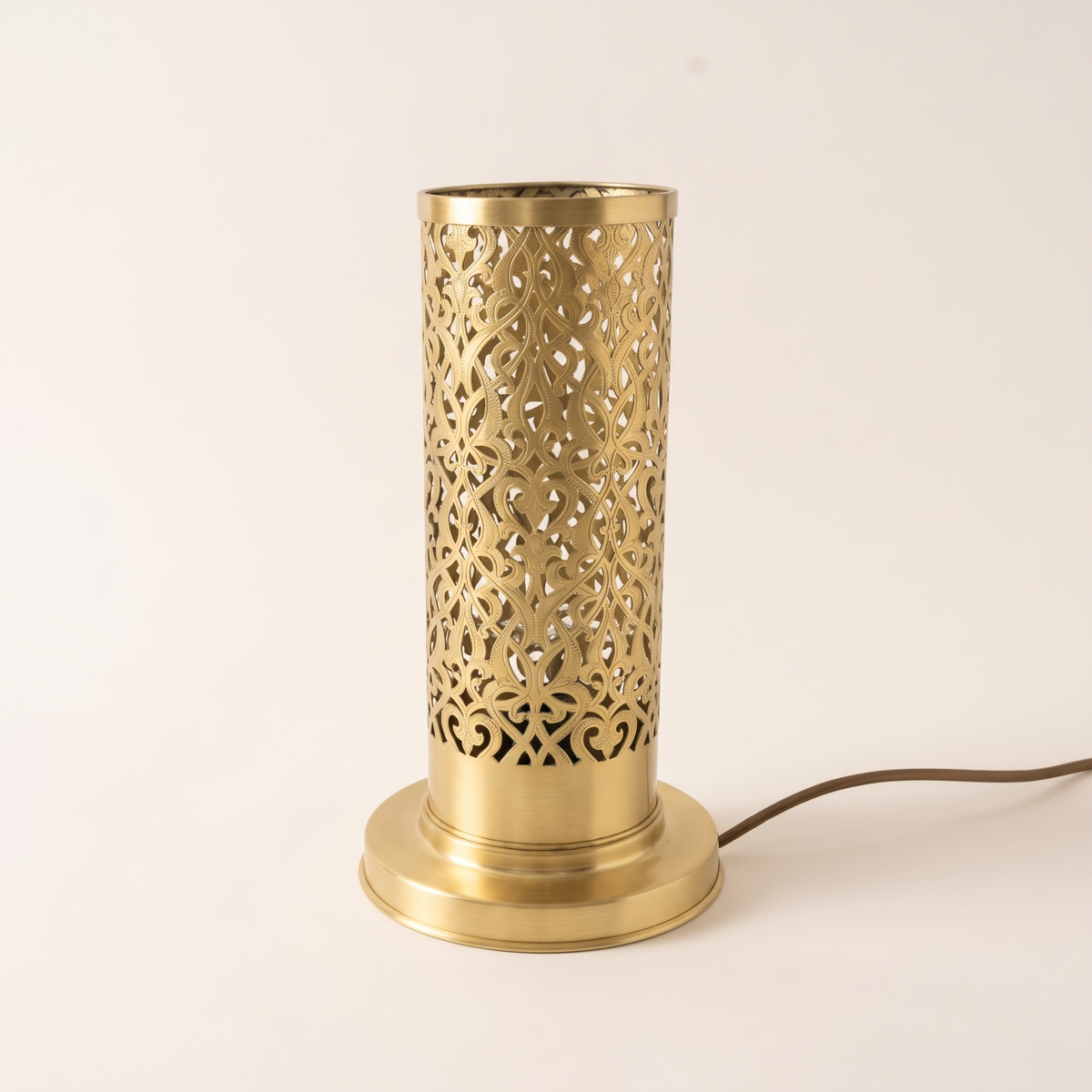 Brushed brass pierced cylinder table lamp with Moroccan pattern on a light background