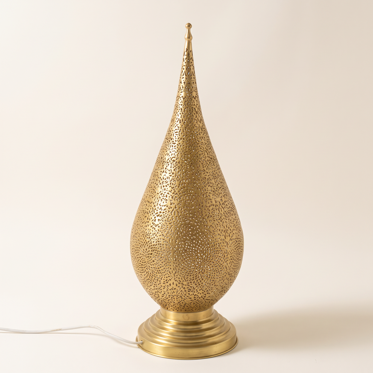 Pierced brass teardrop table lamp with spire top and stepped round base on a light background