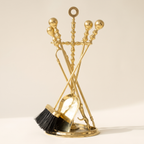 Polished brass fireplace poker set with shovel, brush, poker and tongs on a light background