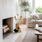Polished brass fireplace tool set with ball handles and half-round stand beside a white plaster fireplace