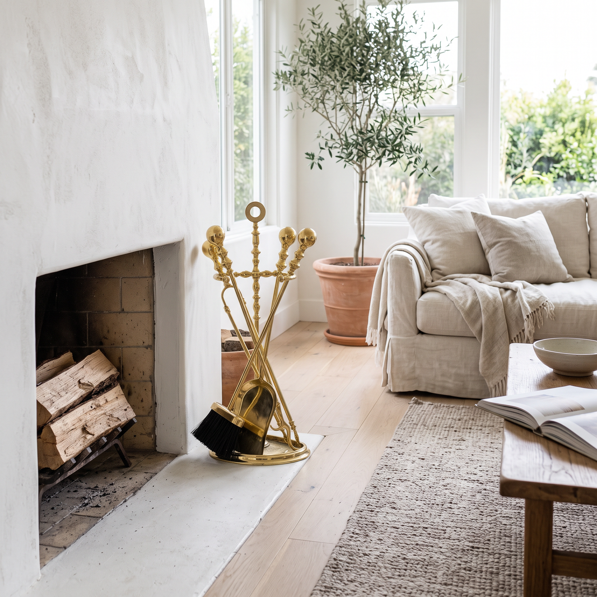 Polished brass fireplace tool set with ball handles and half-round stand beside a white plaster fireplace