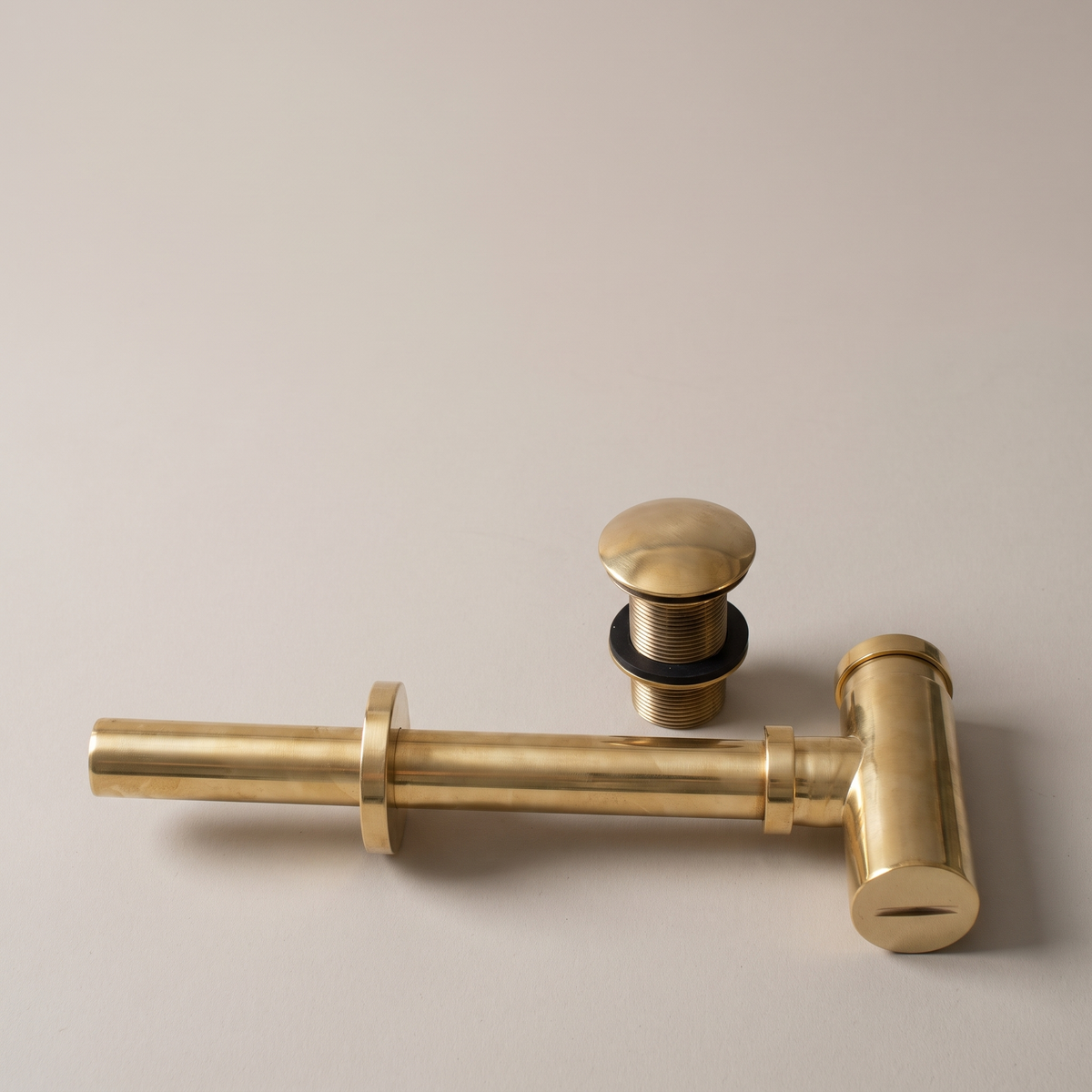 Polished brass round bottle P-trap and push pop-up drain on a light background