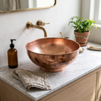 Round copper bowl vessel sink with mottled patina on a white marble vanity with a wall-mounted brass spout